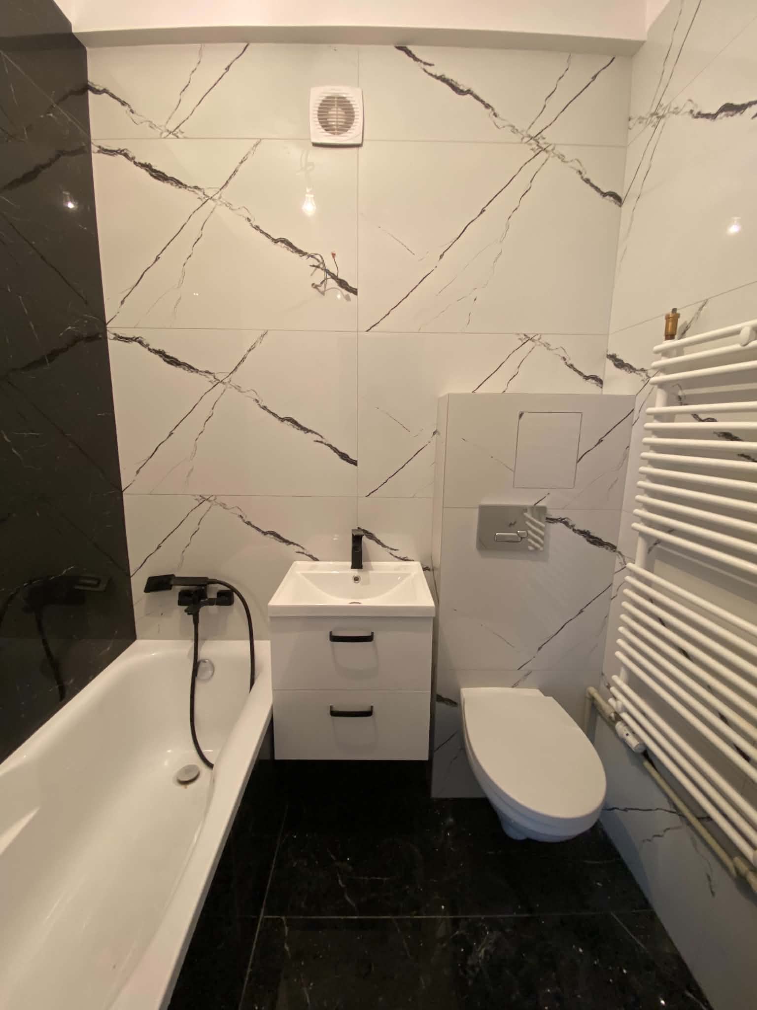 White marble-look tiled bathroom with a bath, wall-hung vanity, toilet and ladder radiator