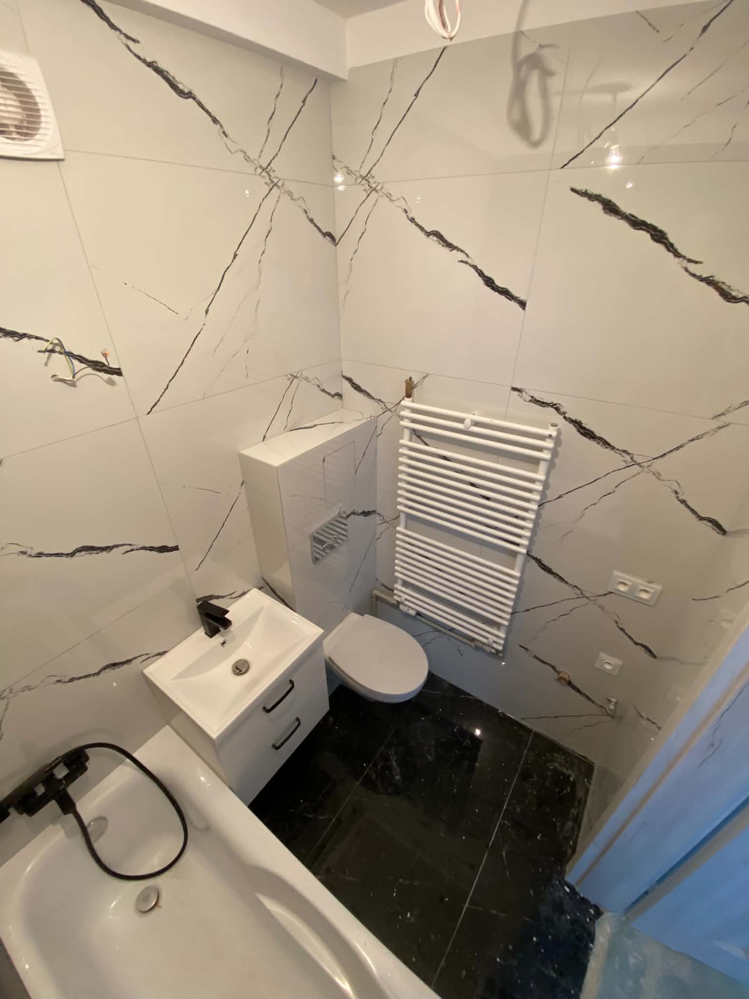 Bath and vanity in a marble-look tiled bathroom with a dark stone-look floor